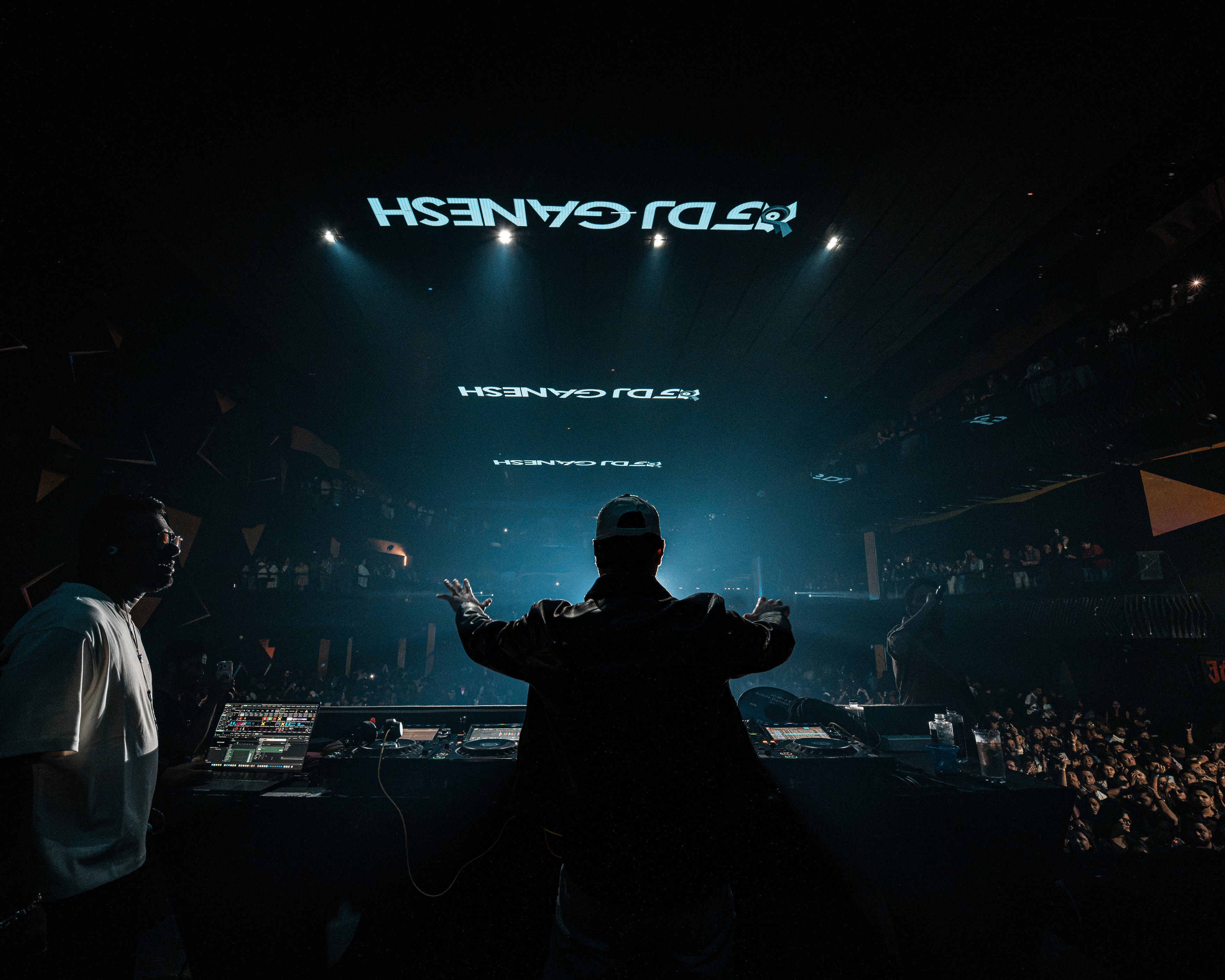 DJ Ganesh at the decks, arms raised to a packed arena, his name on the screens above