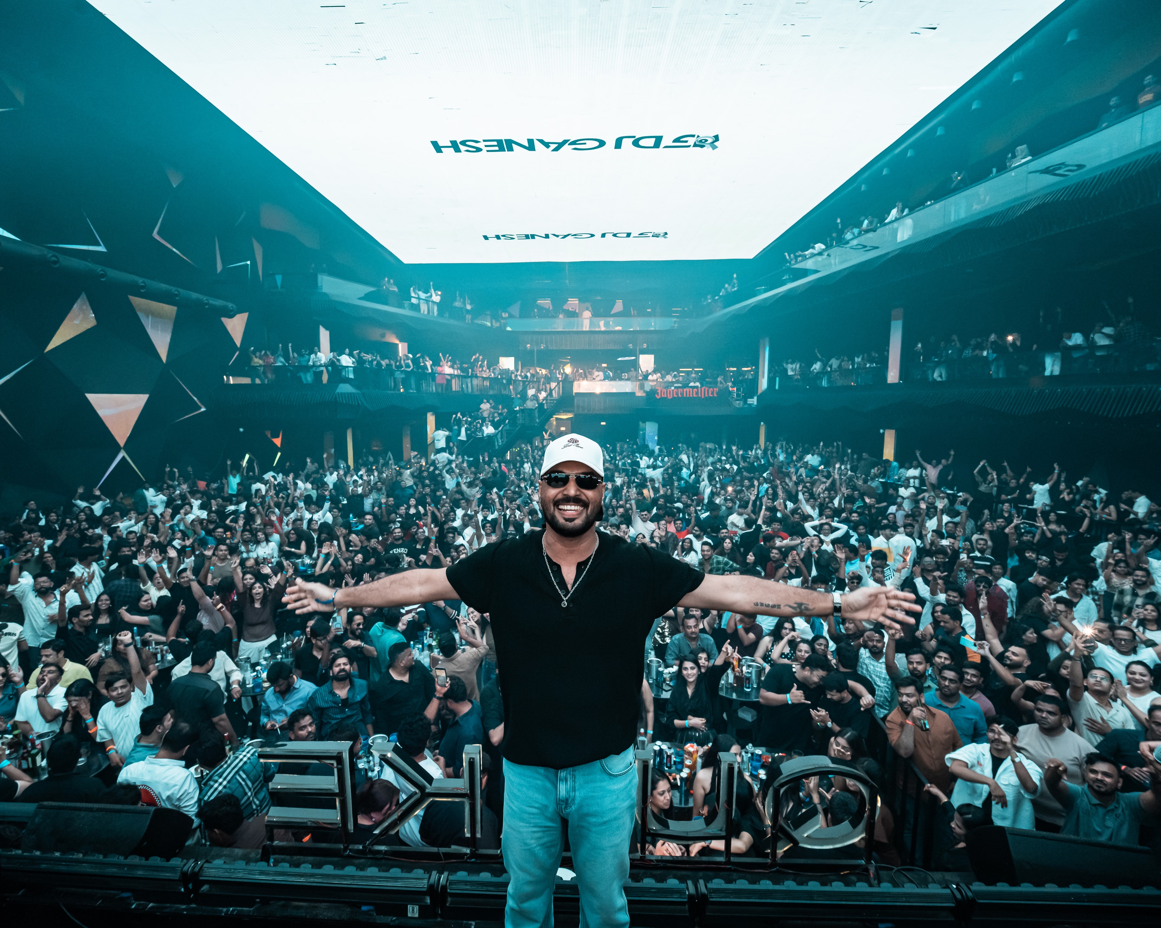DJ Ganesh, arms outstretched, in front of a packed club crowd